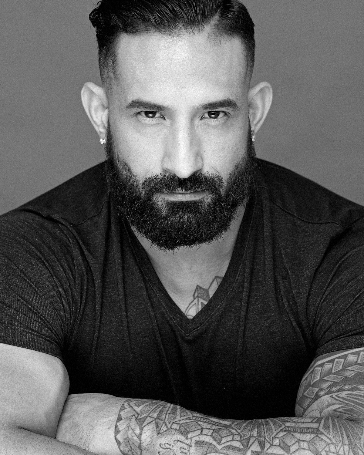 Guy Valentino in a black V-neck T-shirt, arms crossed. Black and white.