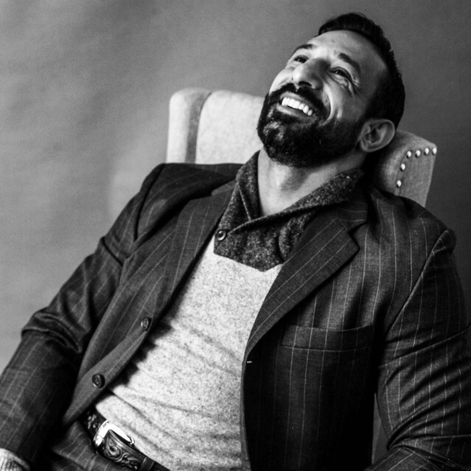 Guy Valentino laughing in a wingback chair, black and white.