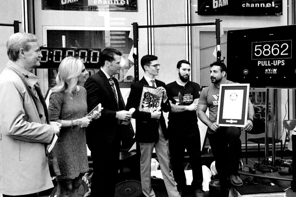 Guy seated on a plyo box holding a framed Guinness World Records certificate, with the Fox & Friends hosts beside him and a screen reading 5862 pull-ups.